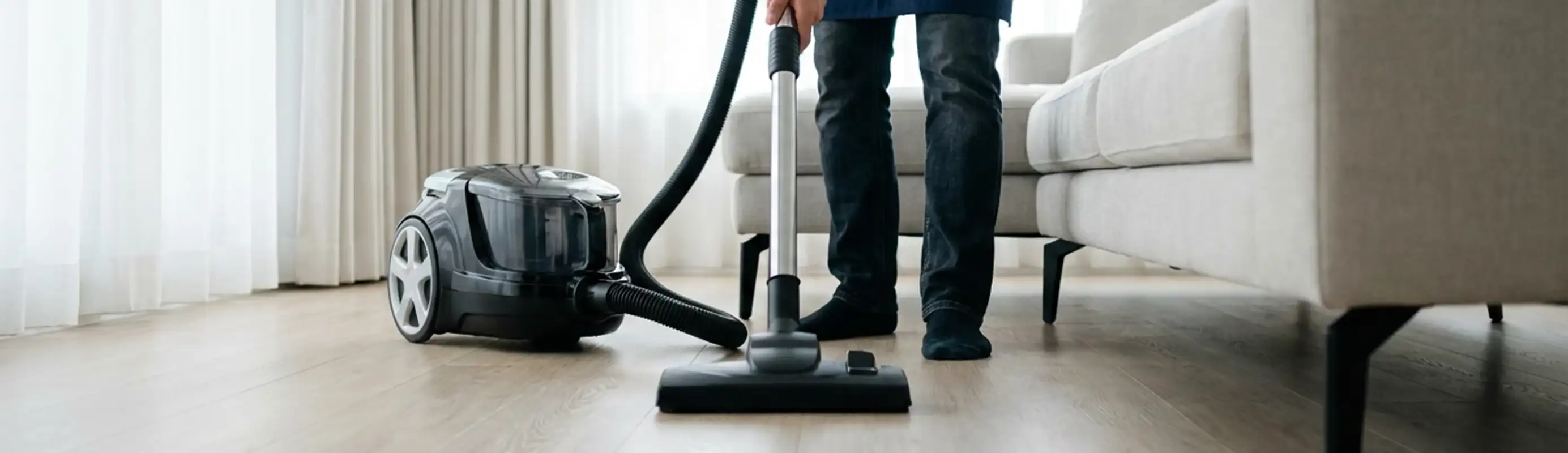 Professional house cleaner vacuuming a living room floor with a canister vacuum cleaner, Anaheim, CA.