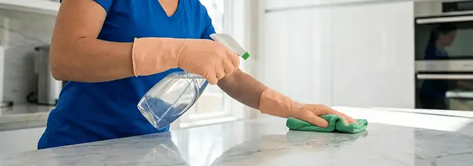 Maid service worker spraying and wiping a kitchen countertop with a microfiber cloth for sanitizing, Anaheim, CA.