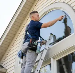Professional window cleaner on a ladder using a squeegee to clean an exterior arched window, Anaheim, CA.