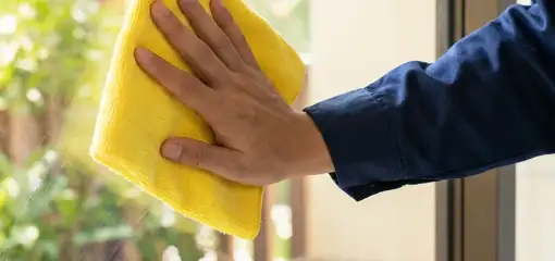House cleaner wiping a glass window with a yellow microfiber cloth for streak-free cleaning, Anaheim, CA.